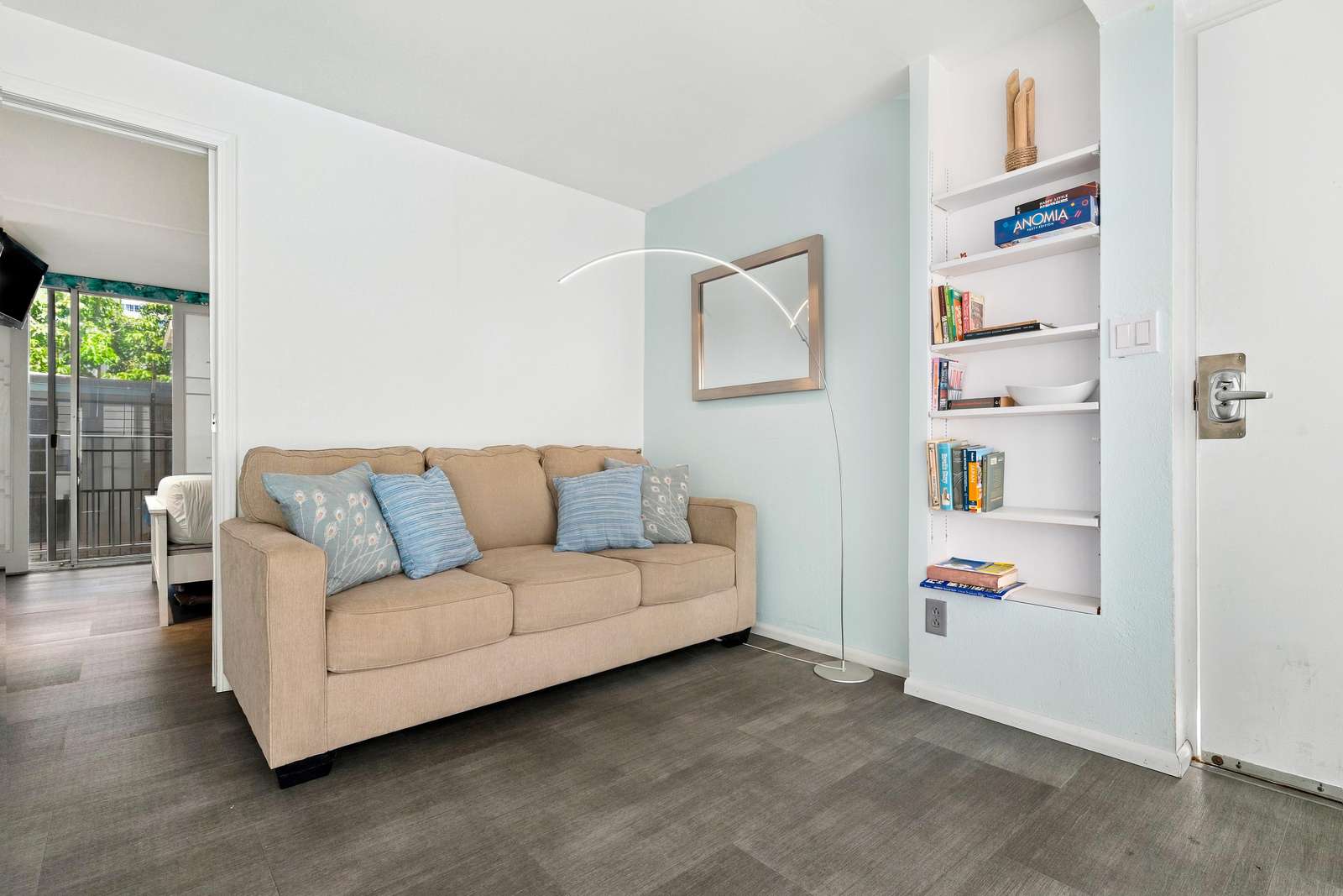 Beige sofa with blue patterned pillows sits beside a built-in white bookshelf and curved floor lamp.