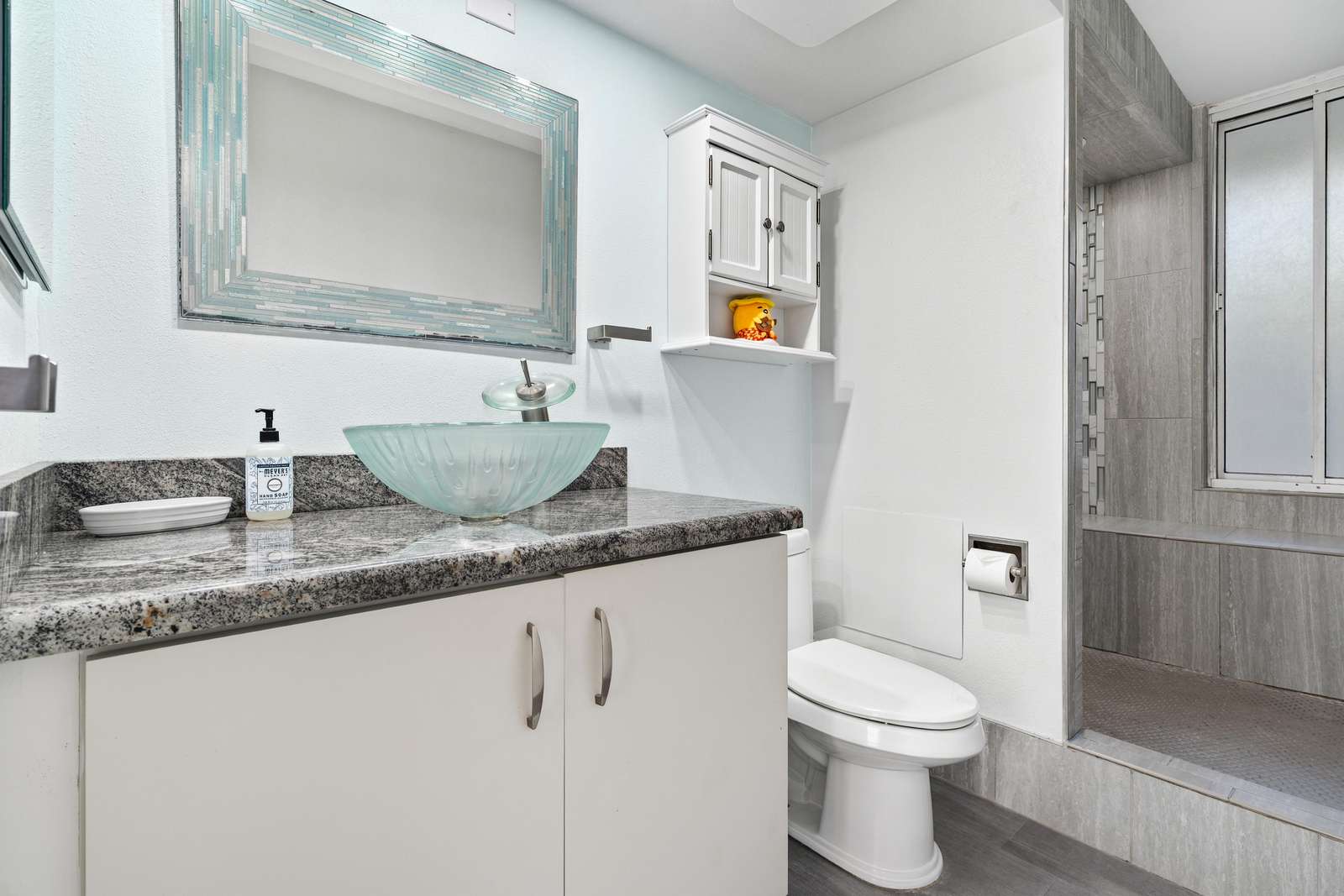 Bathroom features a frosted glass vessel sink on granite countertop, white cabinetry, and gray tiled shower.
