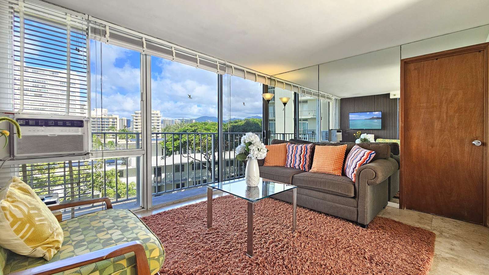 Floor-to-ceiling windows fill the living room with natural light, highlighting a glass coffee table and patterned pillows. - property