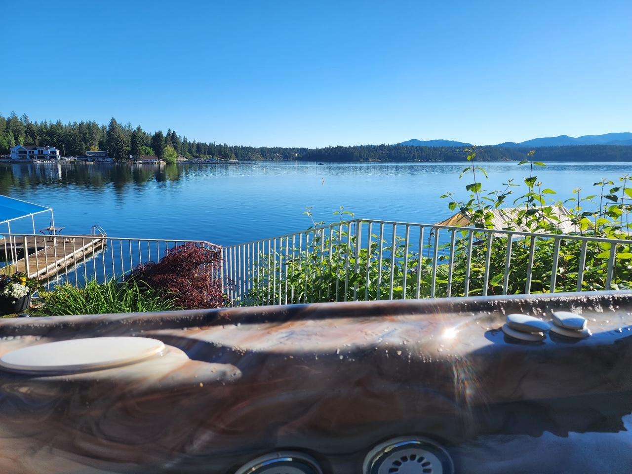 Lakefront hot tub with swirling brown and cream marbled edges overlooks calm water and distant tree-lined shore.