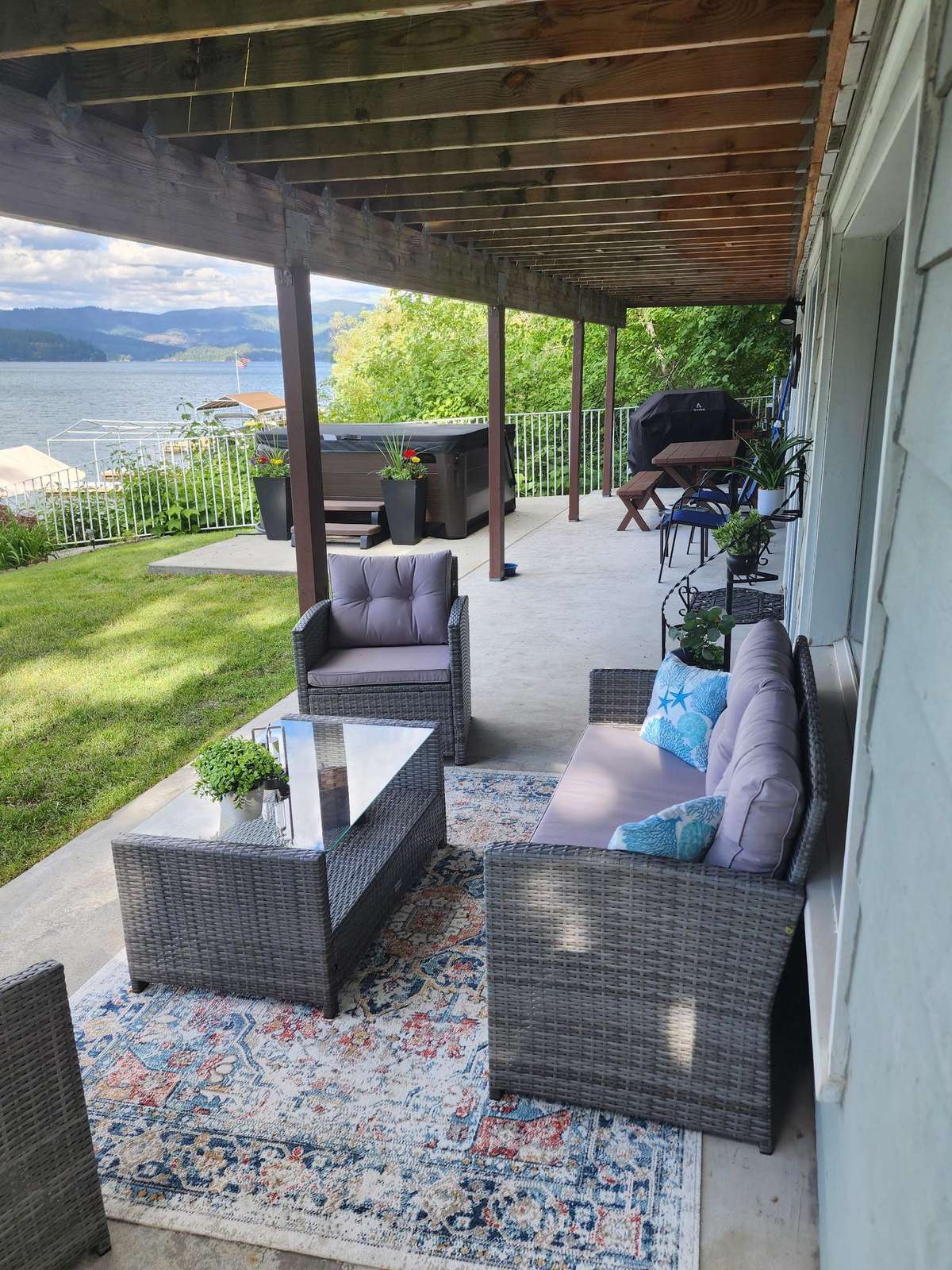 Covered lakeside patio features gray wicker seating with lavender cushions and patterned area rug.