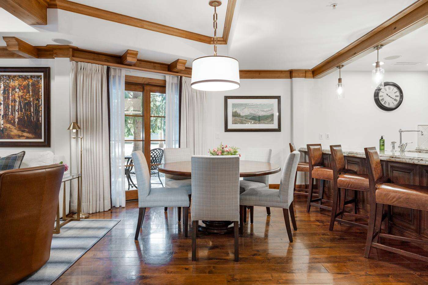 Dining area with round wood table, six gray upholstered chairs, and wood-trimmed ceiling beams. - property