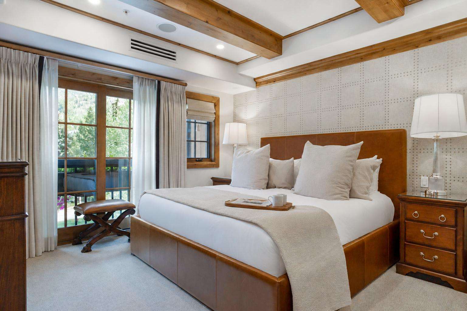 A spacious hotel room with a large bed, wooden furniture, and a balcony with a view of trees.