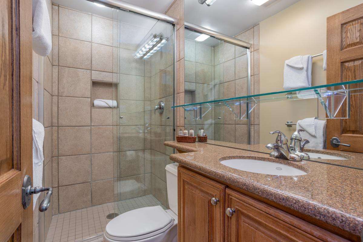 A standard bathroom with a glass-enclosed shower, granite countertop, and wooden cabinets.