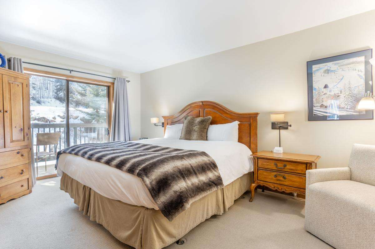 A hotel room with a bed, nightstand, chair, and sliding glass doors leading to a balcony.