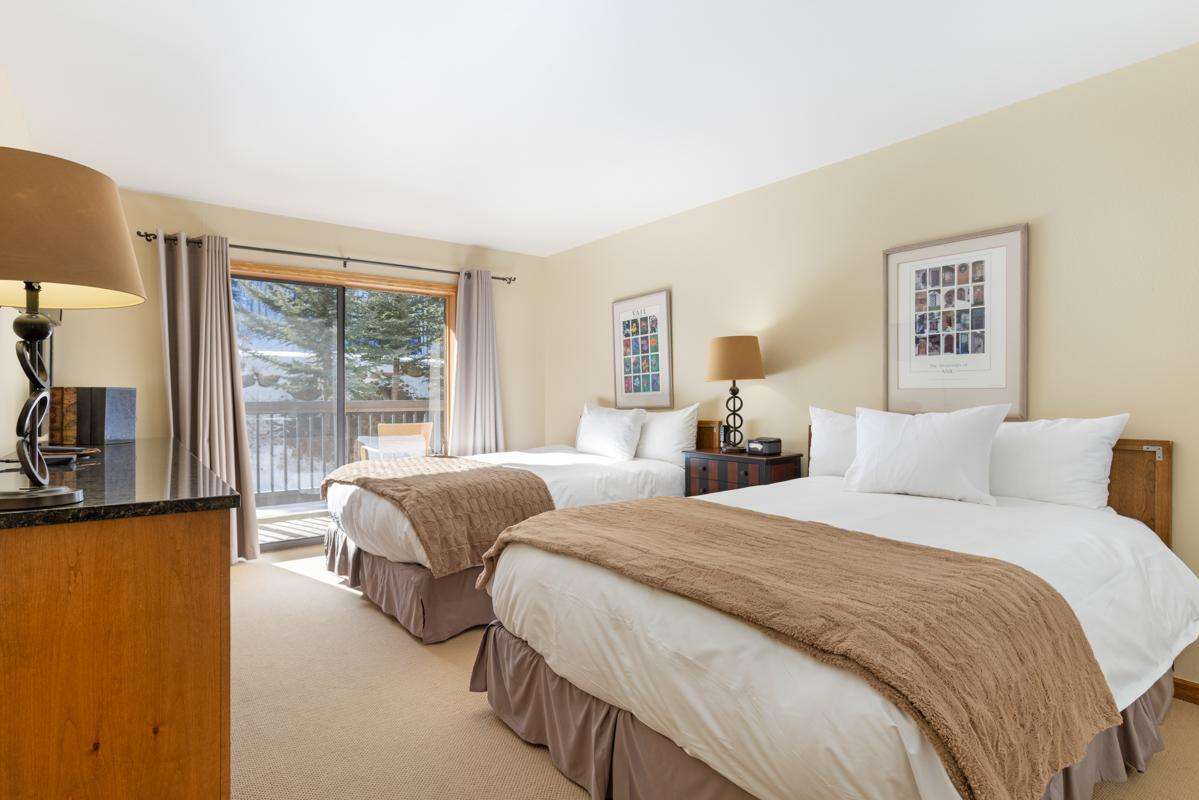 A hotel room with two double beds, a carpeted floor, and a sliding glass door leading to a balcony.