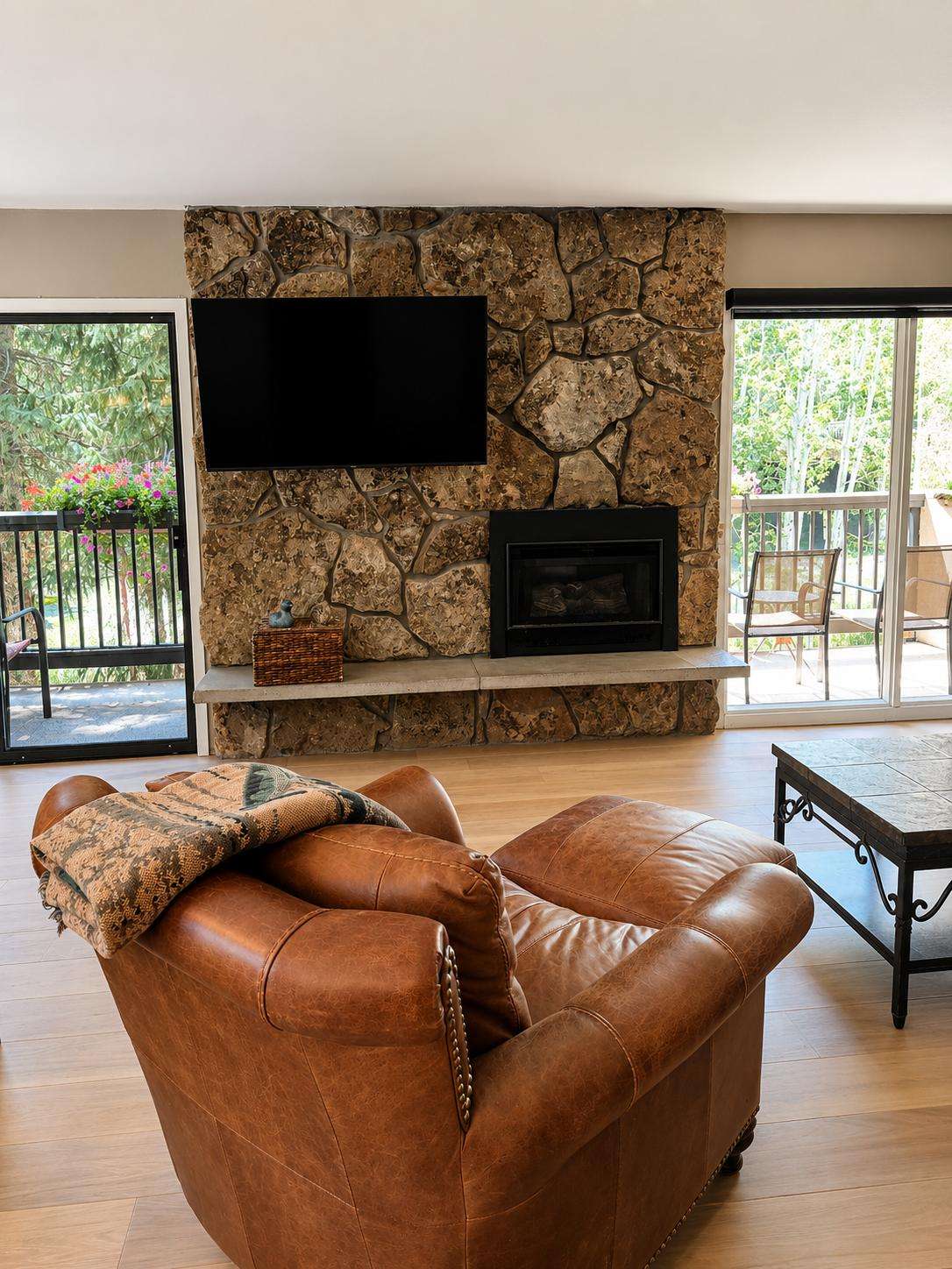 A cozy living room with a stone fireplace, leather sofa, and sliding glass doors leading to an outdoor patio.