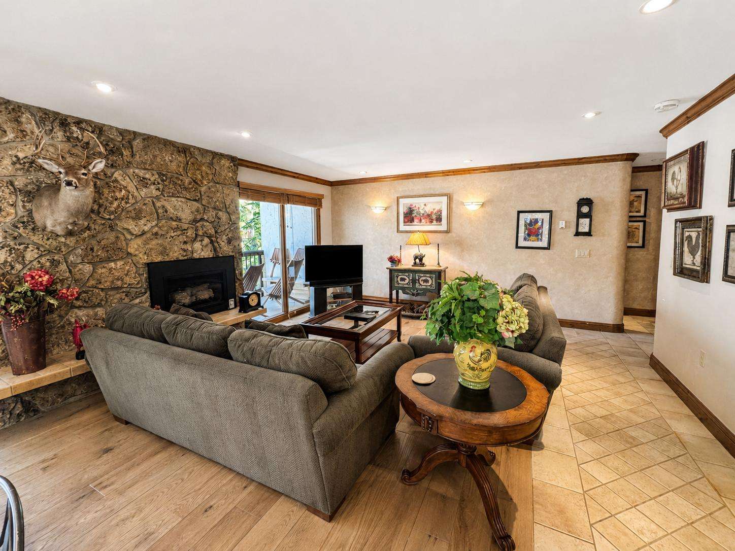 Living room with gray upholstered sofas, stone fireplace, hardwood floors, and sliding glass door to balcony. - property