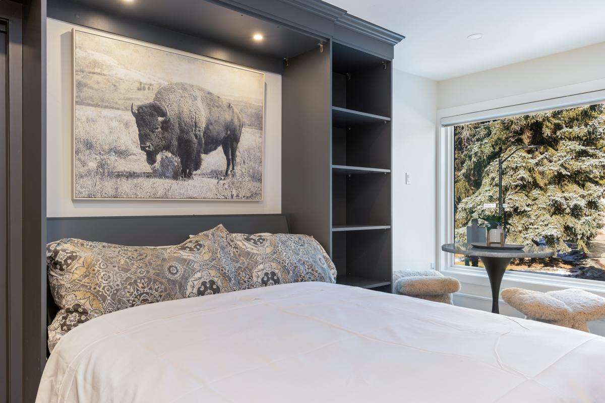 A bed with pillows and a large picture of a bison on the wall above it, with a window and table in the background.