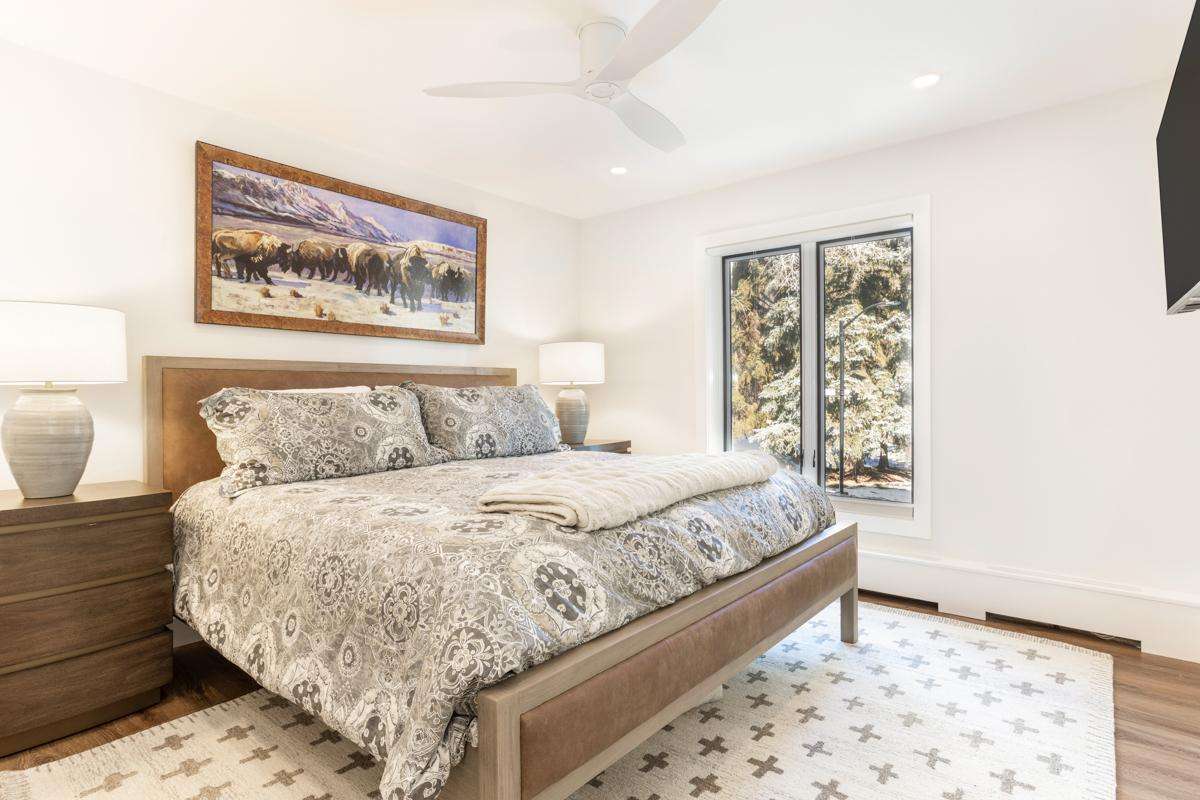 A wide view of a bedroom with a bed, nightstands, lamps, and a window.