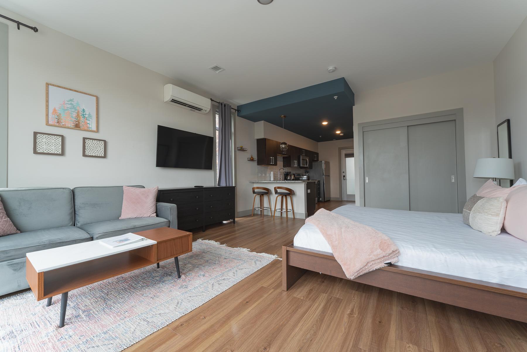 A wide view of a studio suite with a sofa, kitchenette, and bed.