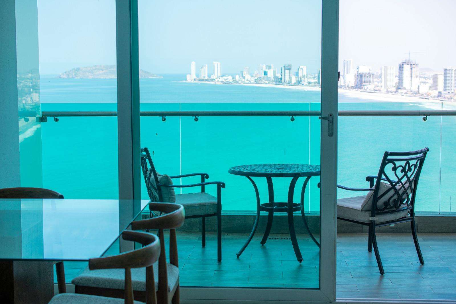Glass sliding doors open to a balcony with wrought iron chairs and a round table overlooking the ocean and city skyline. - property