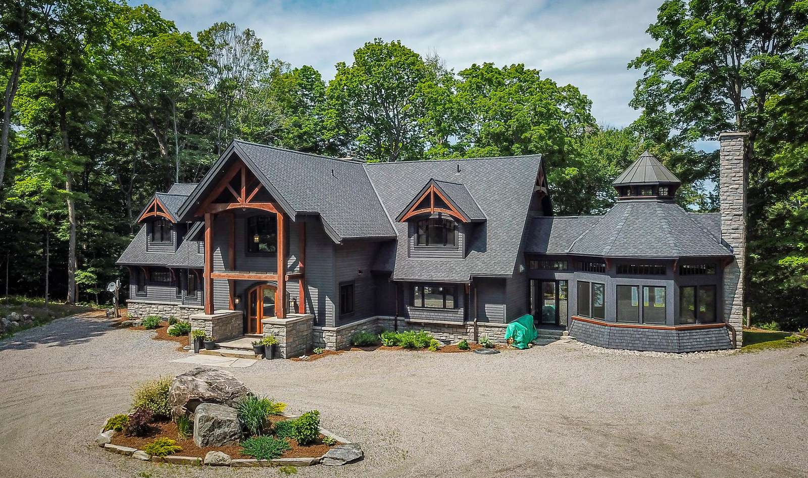 Front exterior of the cottage showcases dark gray shingles, stone accents, and wooden beams framing the covered entryway.