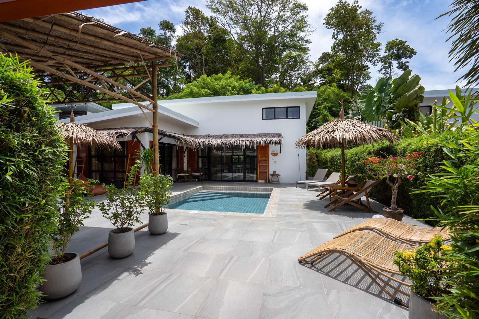 Gray tile patio surrounds a small blue-tiled pool, with rattan loungers and thatched umbrellas nearby. - property
