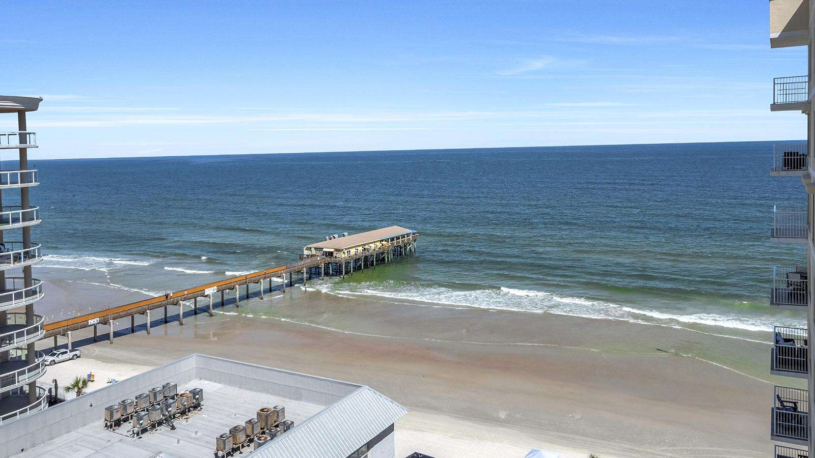 Oceanfront view from the balcony showing a wooden pier extending over sandy beach and gentle waves. - property
