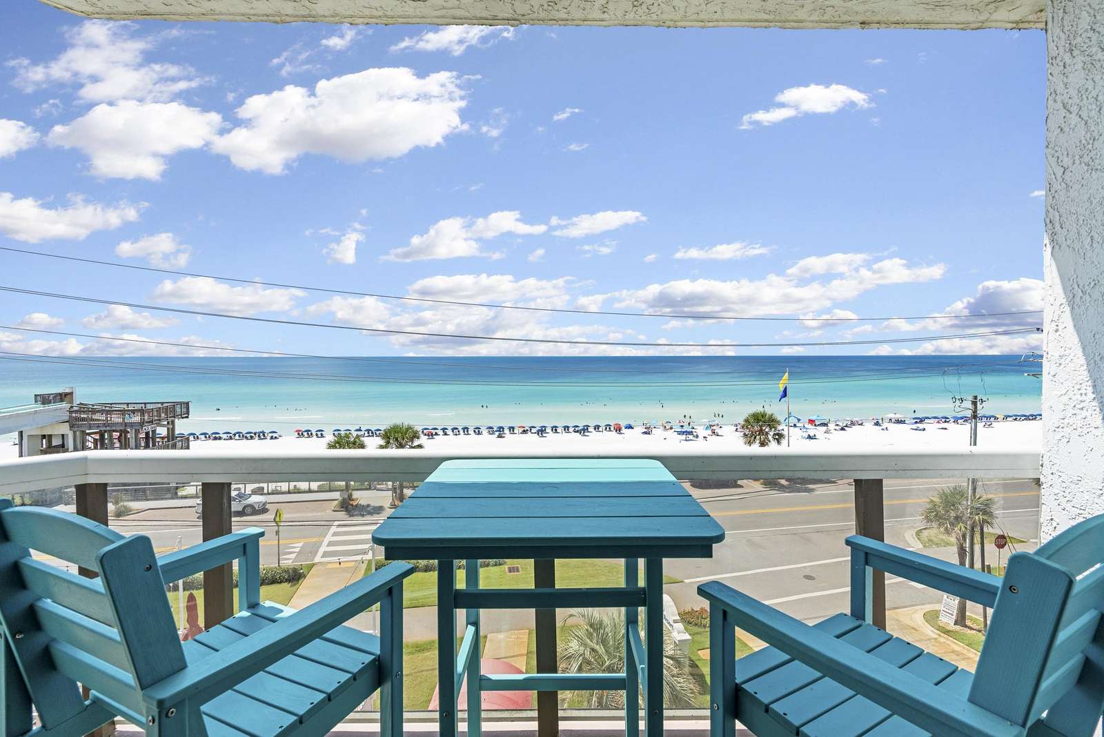 Balcony with turquoise wooden chairs and table overlooks white sand beach and turquoise ocean under a blue sky. - property