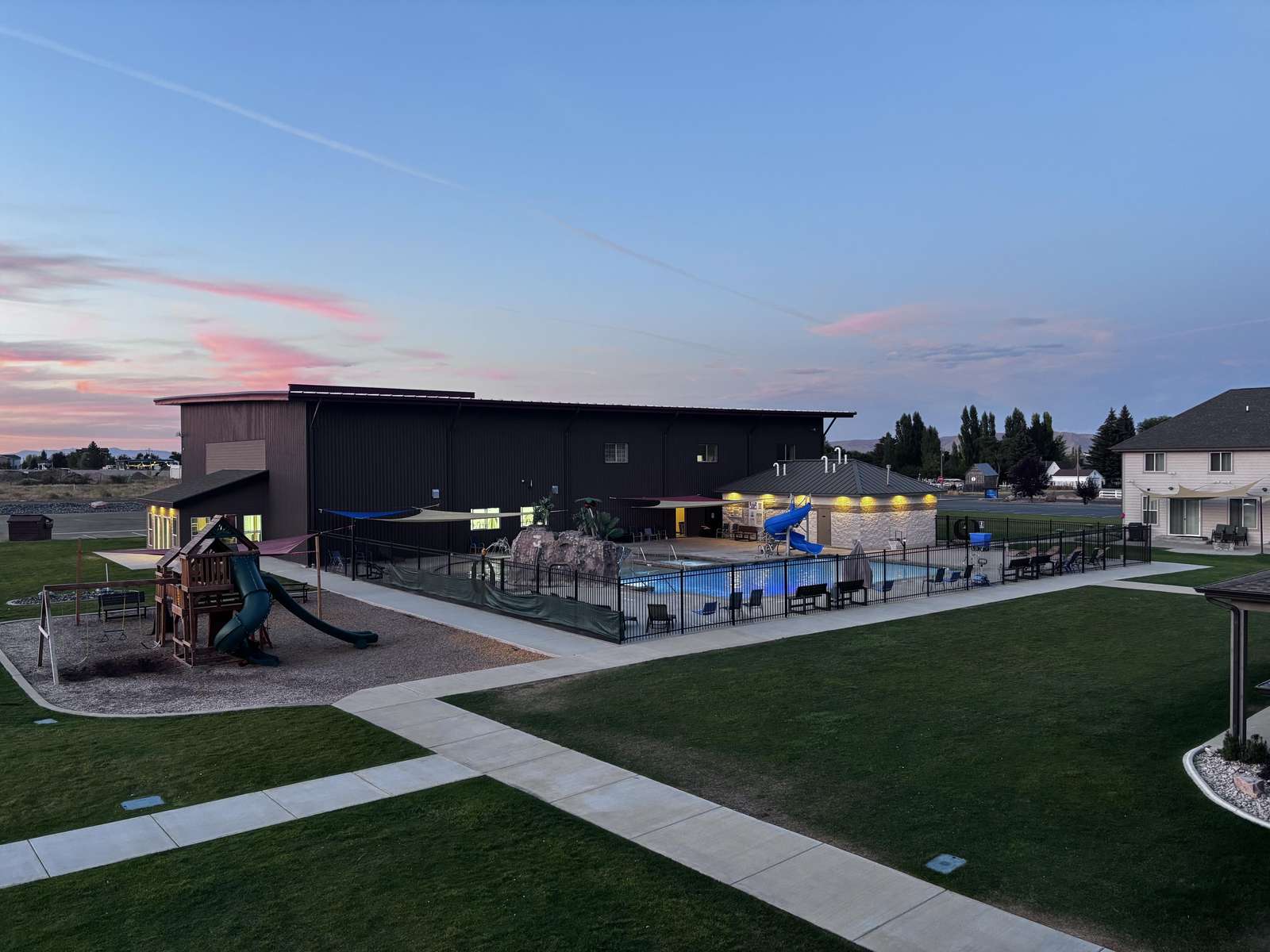 Evening view of the fenced outdoor pool area with blue slide, rock water feature, and shaded lounge seating. - property