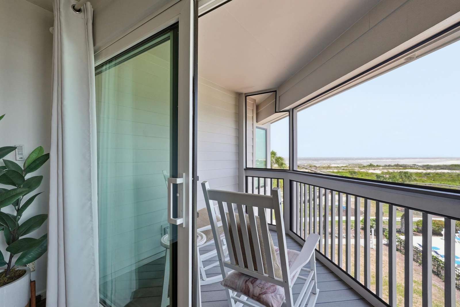 Screened porch with white rocking chairs overlooking dunes and ocean beyond the black railing. - property