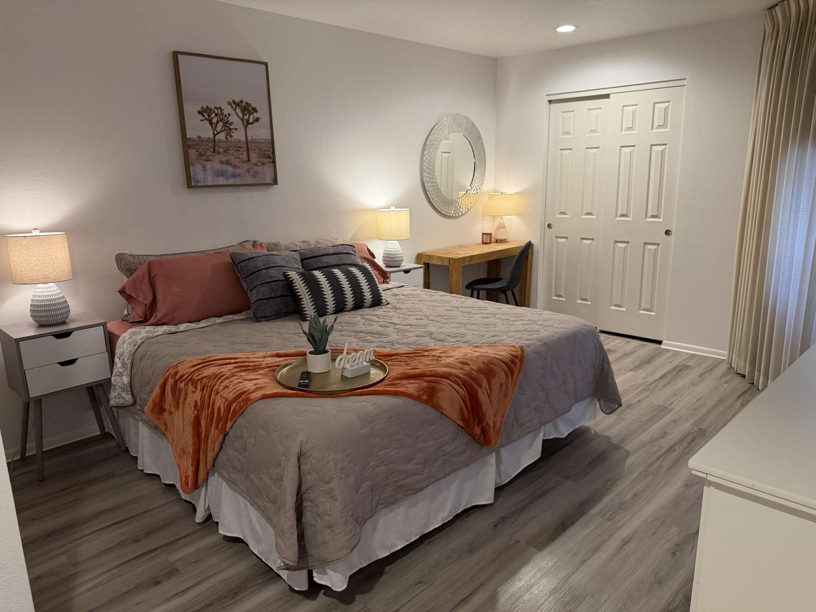 Queen bed with layered pillows and rust throw, flanked by white nightstands and lamps on vinyl plank flooring. - property