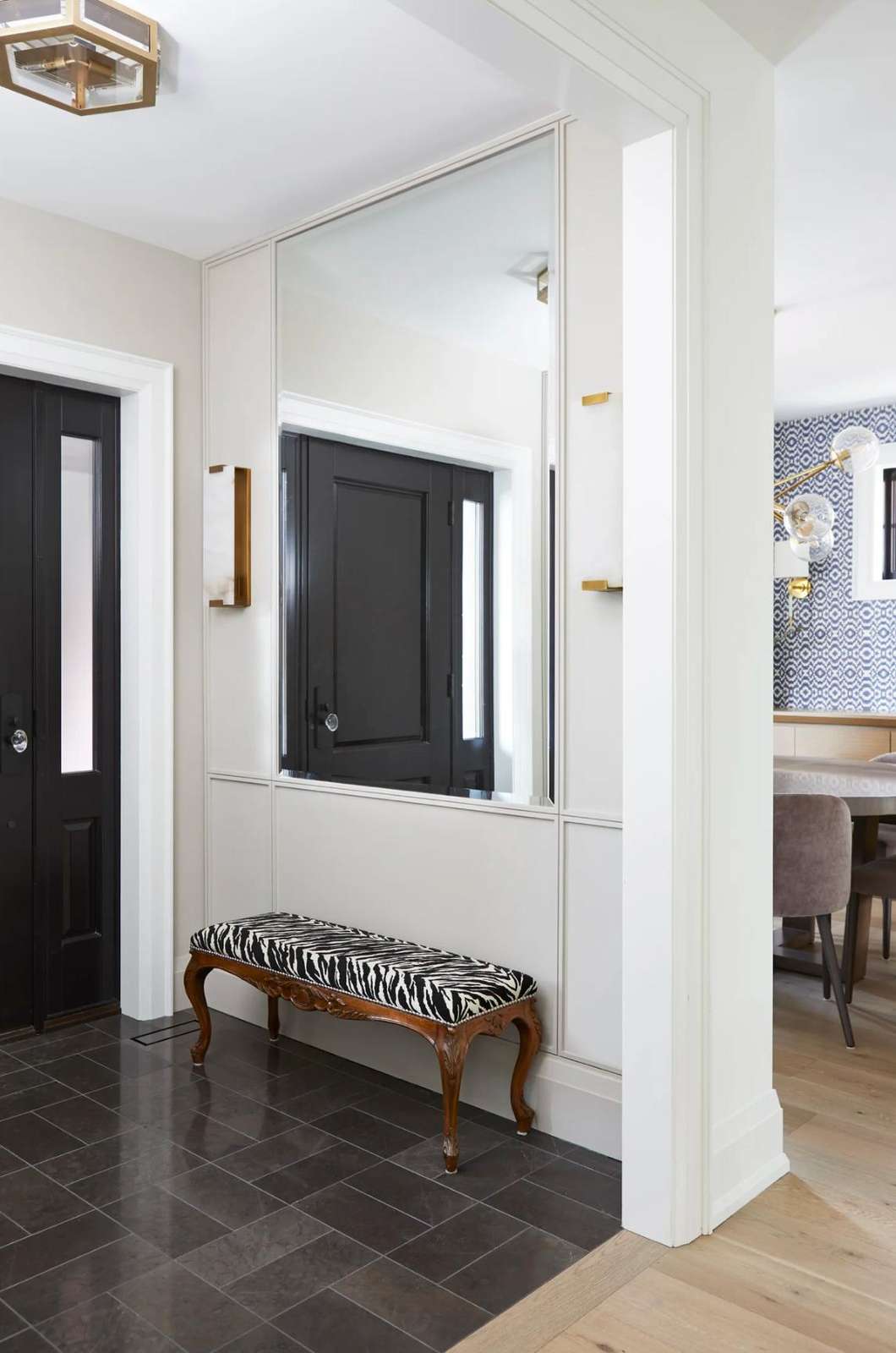 Entryway with glossy black tiled floor, carved wood bench upholstered in zebra print, and large wall mirror.