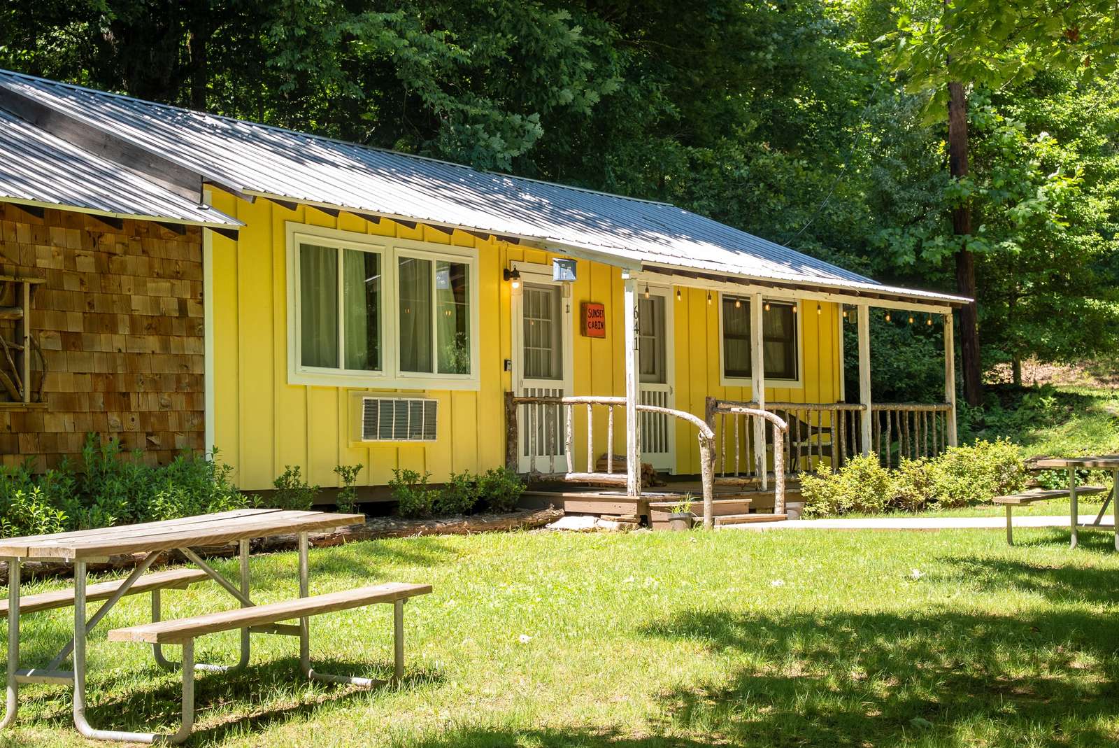 Yellow cabin exterior with a metal roof, rustic porch railing, and wooden picnic tables on green lawn. - property