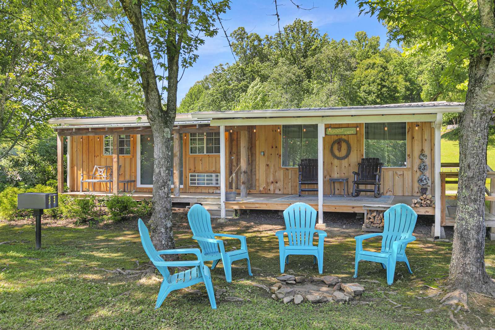 Blue Adirondack chairs circle a stone firepit on the grassy yard in front of the wood-paneled cabin porch. - property