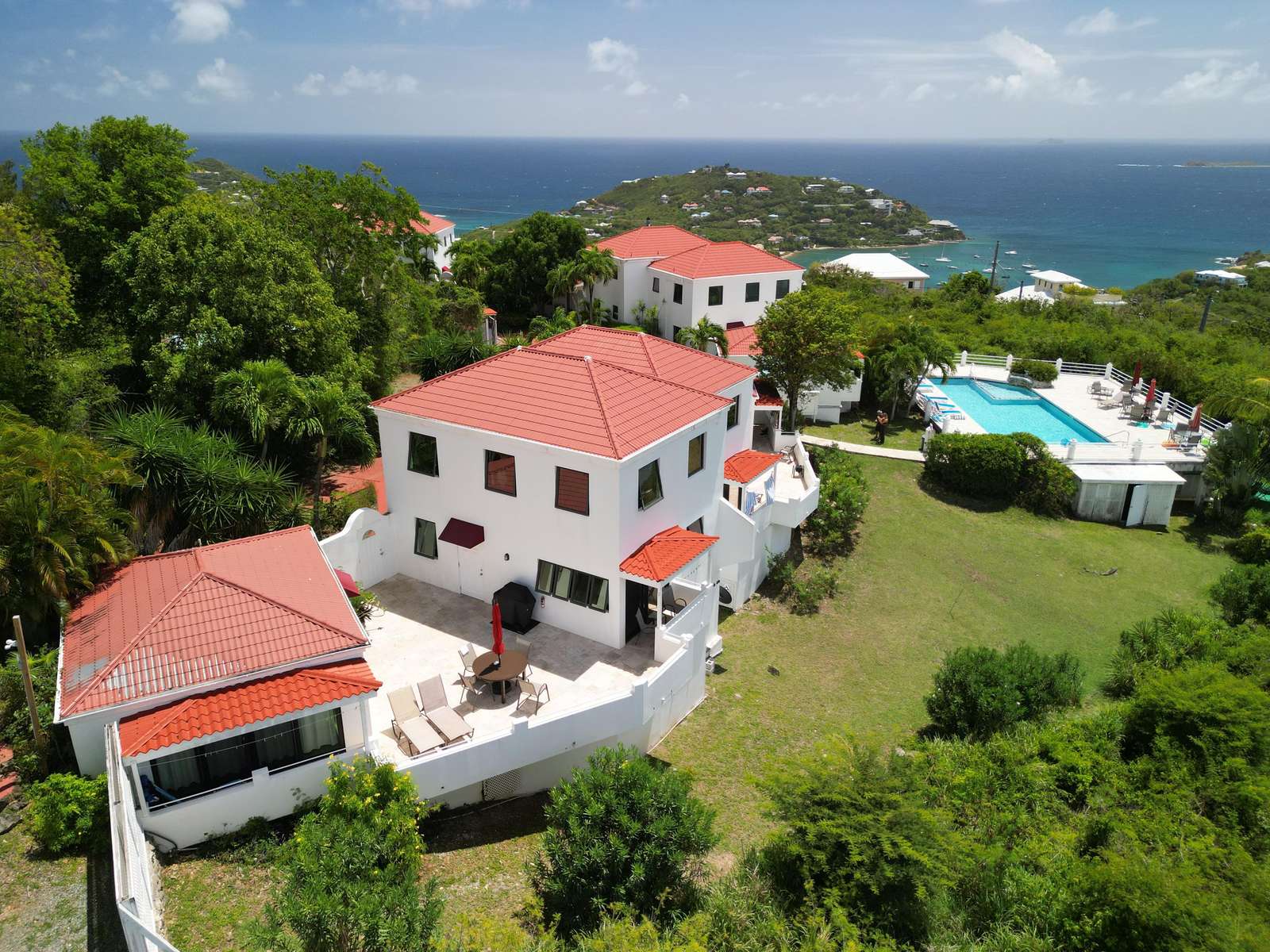 Aerial view of white stucco villa with red tile roofs, spacious patio, pool, and ocean backdrop. - property