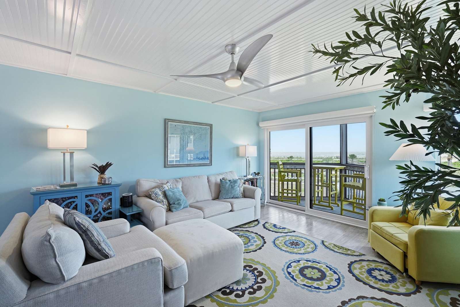 Living room with pale blue walls, patterned area rug, sliding glass doors opening to balcony seating. - property