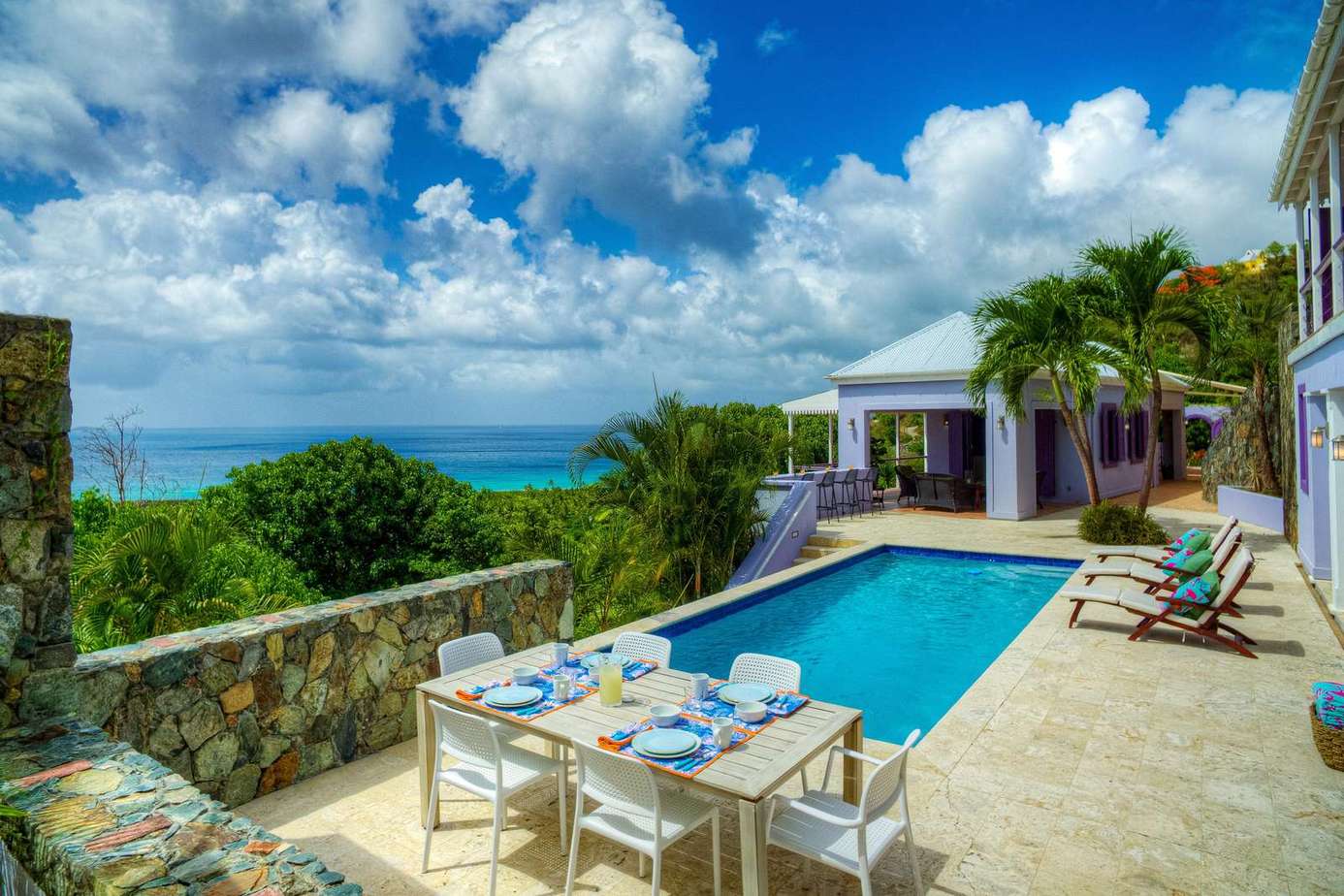 Sunlit poolside patio with stunning ocean views and dining area