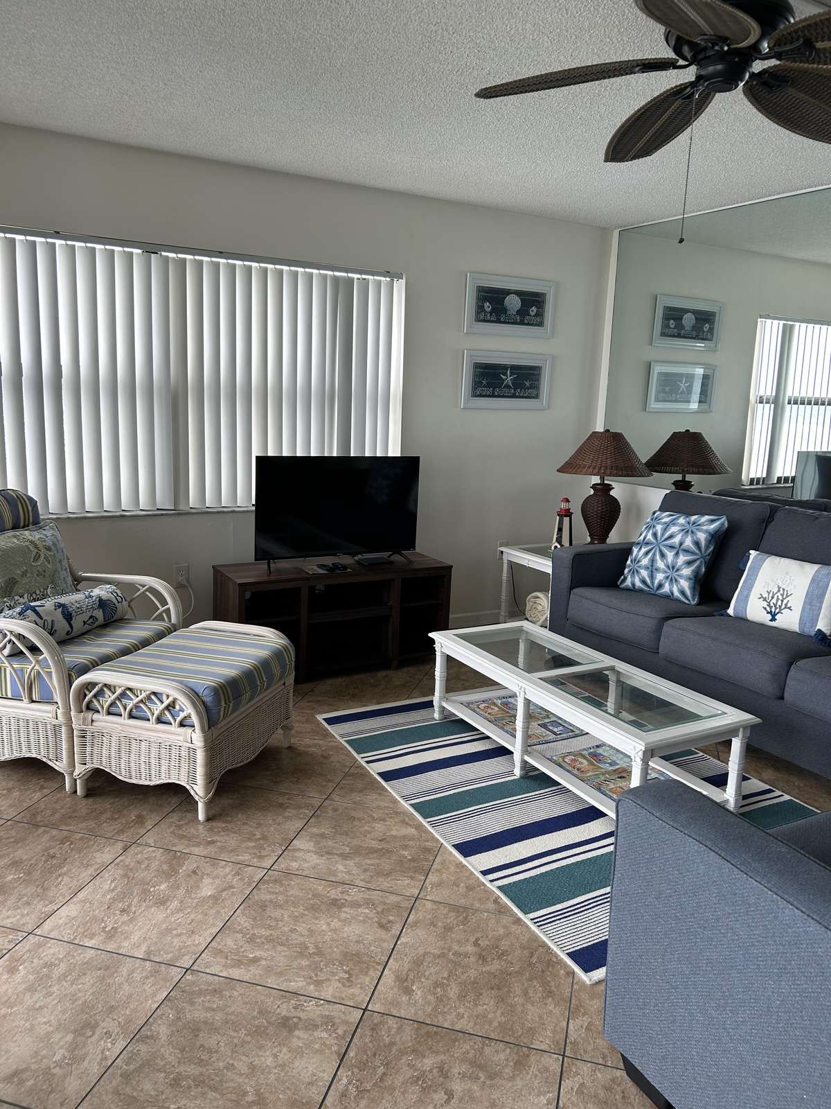 Living area features tiled floors, a striped rug, wicker armchair with ottoman, and a blue-gray sofa. - property