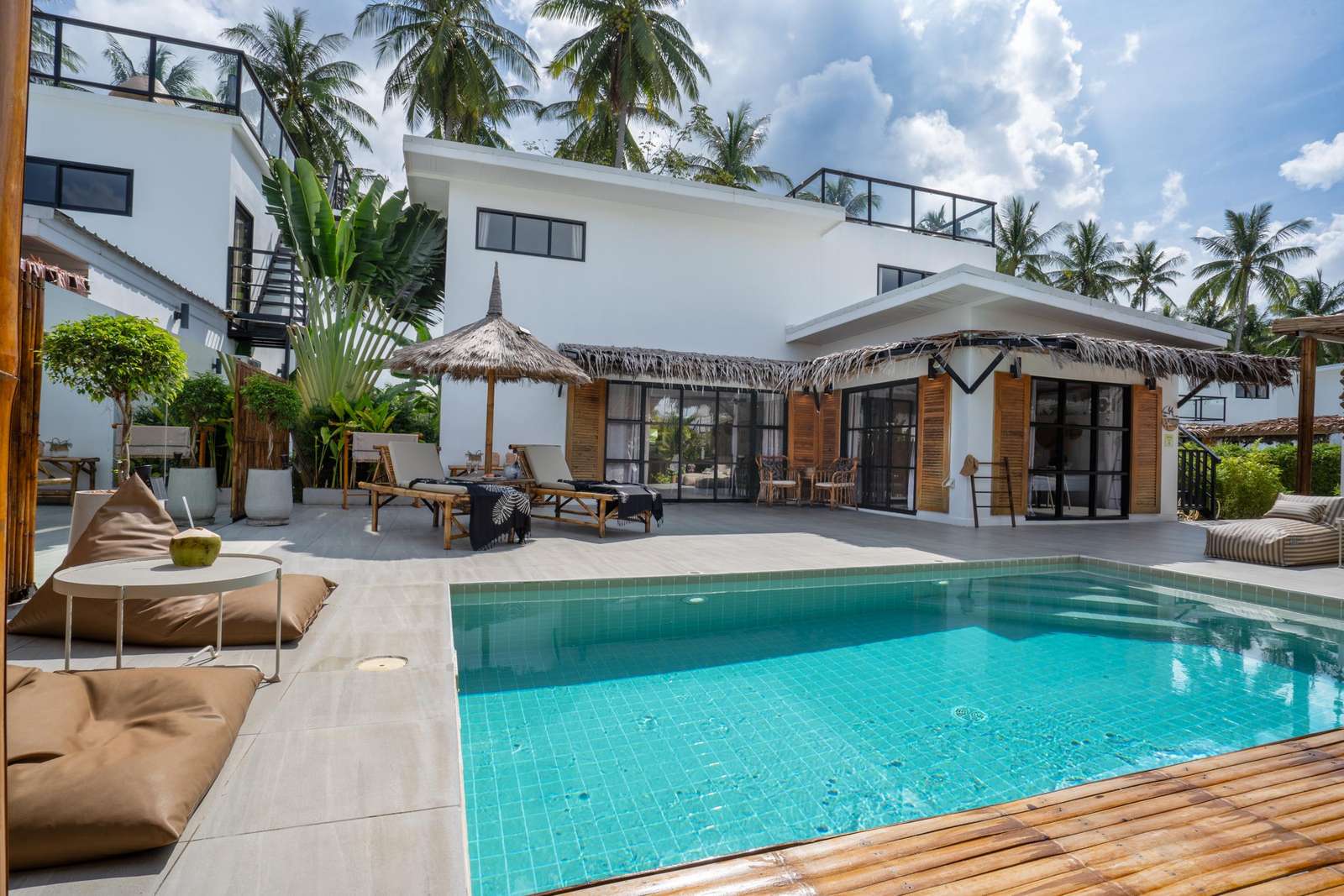 A turquoise-tiled pool sits beside tan loungers, bean bags, and a modern white villa with wooden shutters. - property
