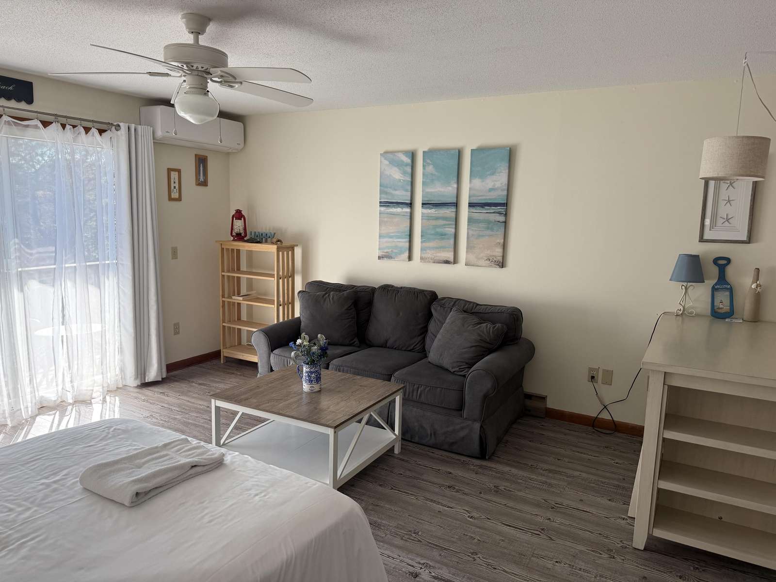Natural light filters through sheer curtains onto the gray sofa, wood coffee table, and rustic plank flooring. - property